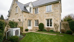 Maison individuelle française en rénovation avec une pompe à chaleur air-eau extérieure discrètement installée dans le jardin.